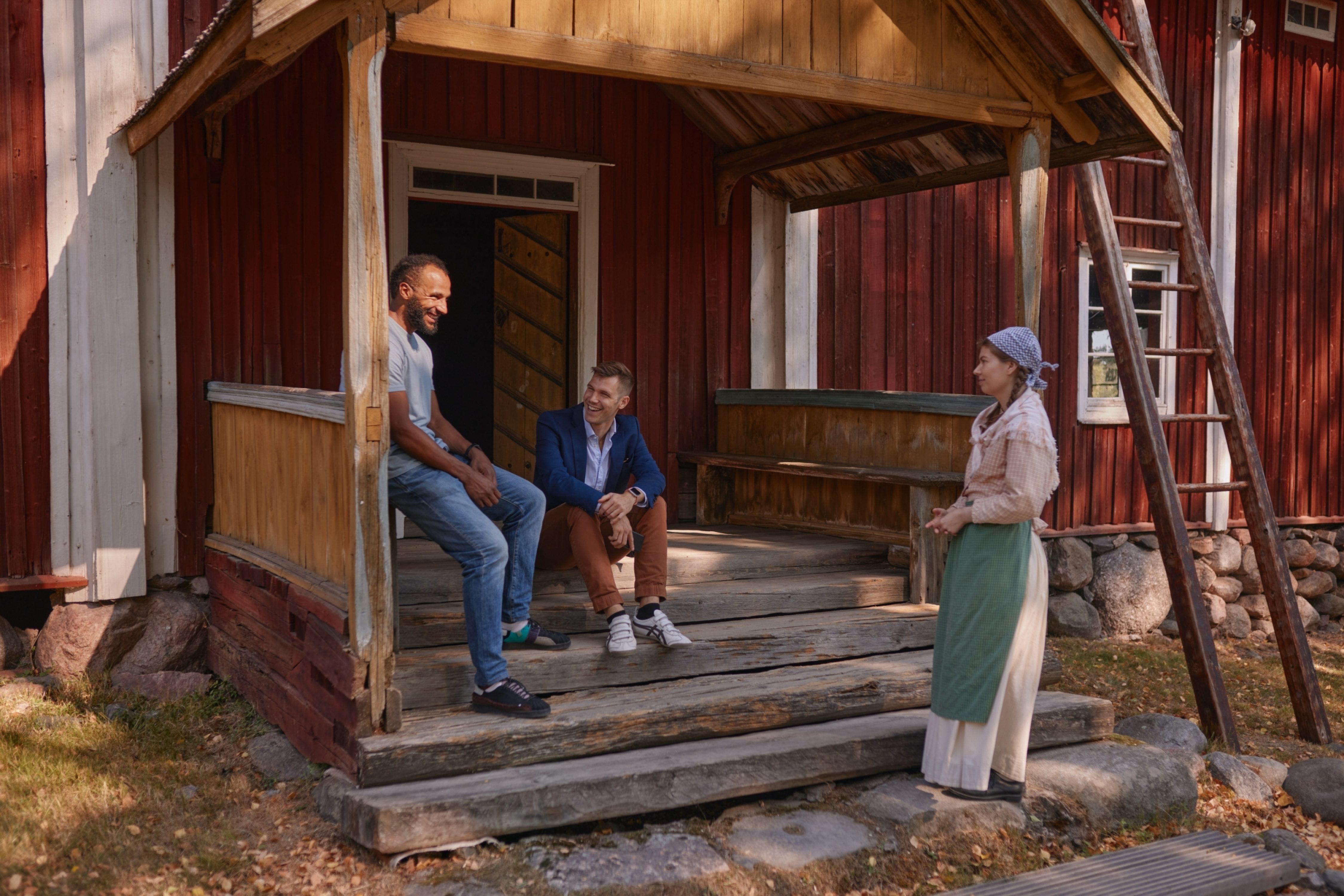 Kolme henkilöä juttelemassa talon kuistilla. Kuva: Sanna Lehto, Suomen kansallismuseo